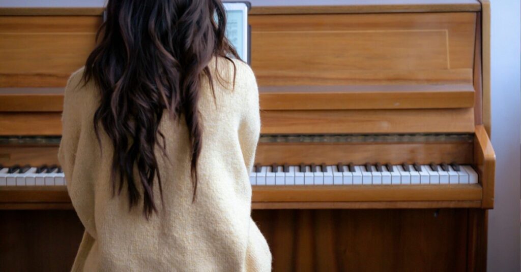 self value as a christian woman. This picture shows a young woman with flowing brown hair sitting at a piano. It emphasises the striving felt to be achieving in all the right spheres as a christian woman.